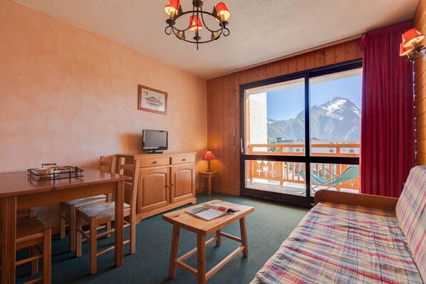 Una habitación acogedora con un escritorio de madera, televisor, sofá y un amplio ventanal con vistas a la montaña.
