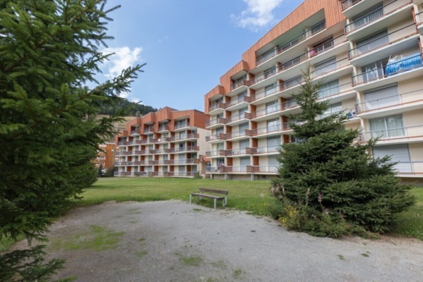 A multi-story residential building with balconies, a gravel path, and greenery.