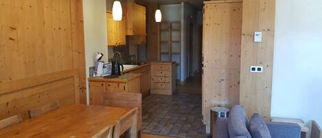 A wooden interior with a dining table, kitchen area, and a sofa.
