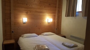 Une chambre d’hôtel avec une tête de lit en bois, deux tables de chevet, un lit avec du linge de lit blanc et deux lampes fixées au mur.