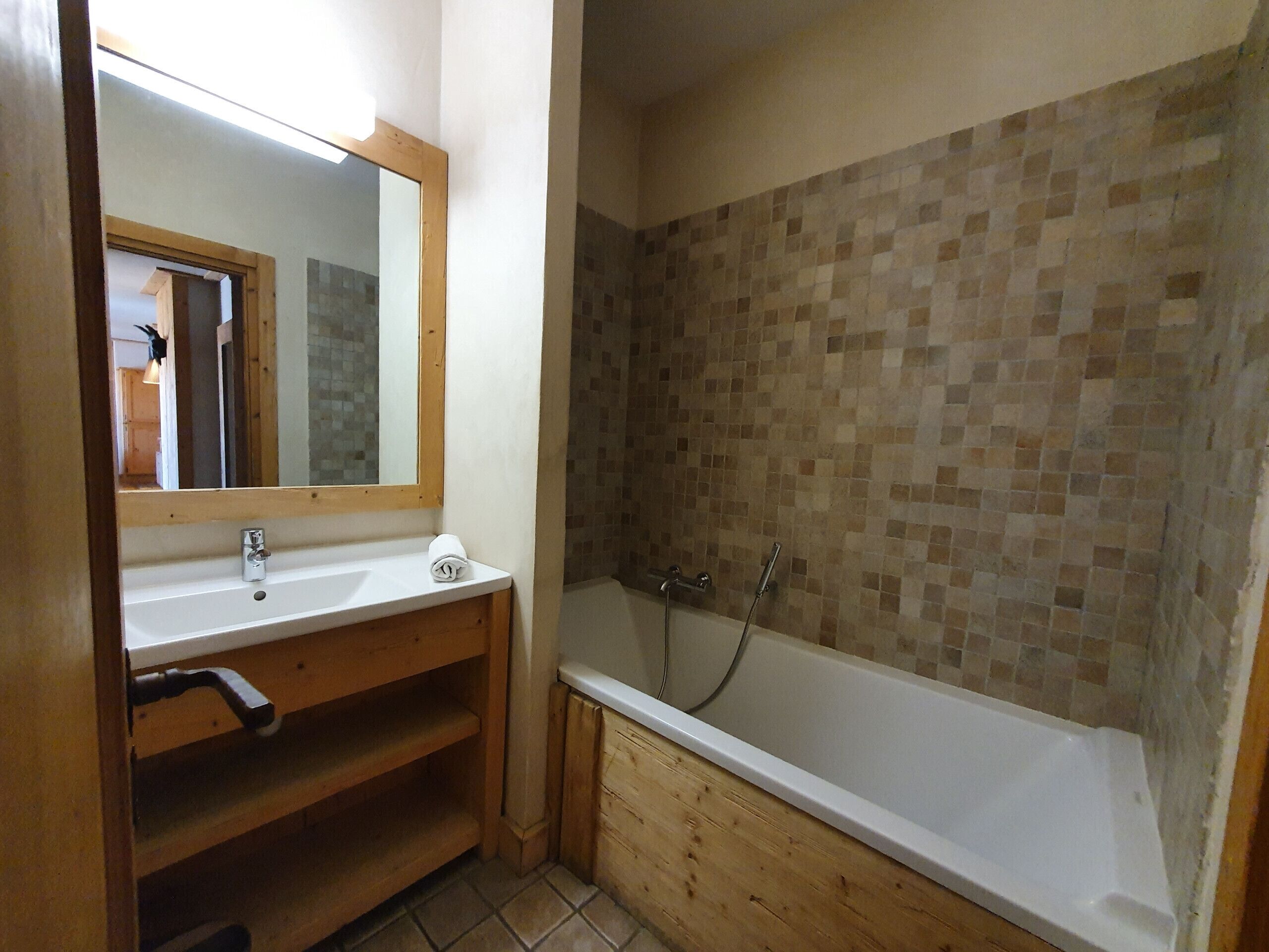 Un baño con tocador de madera, un espejo, un lavabo, una bañera y una pared de ducha con azulejos.