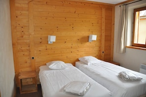 A room with two beds, wooden walls, a window with curtains, and two wall-mounted light fixtures. - Premium flat with a terrace offering mountain views (Les Deux Alpes)