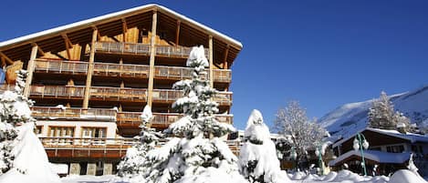 Un edificio de madera de varios pisos con balcones, rodeado de árboles cubiertos de nieve y un cielo azul despejado.