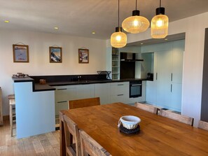 Une cuisine moderne dotée d’un îlot central, de luminaires suspendus et d’un coin repas avec une table et des chaises en bois.