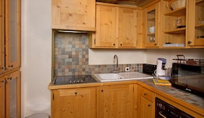 Cozinha com armários de madeira, painel de azulejos, pia, cafeteira e micro-ondas.