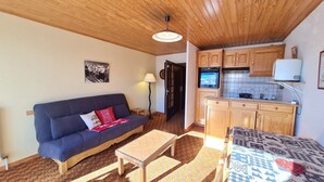 Una sala de estar acogedora con un sofá, una mesita y una cocina con alacenas de madera y salpicadero de azulejos.
