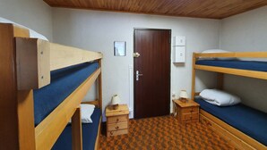 Un dormitorio con literas, techo de madera, tragaluz, puerta, mesita de noche pequeña con lámpara y alfombra estampada.