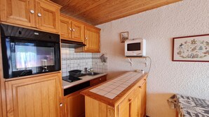 Una cocina compacta con armarios de madera, horno integrado, microondas y salpicadero de azulejos.