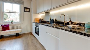 Et moderne køkken med hvide skabe, en marmorbordplade og en indbygget ovn.