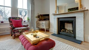 En stue med pejs, en blomstret lænestol, en rød sofa og et sofabord med glas.