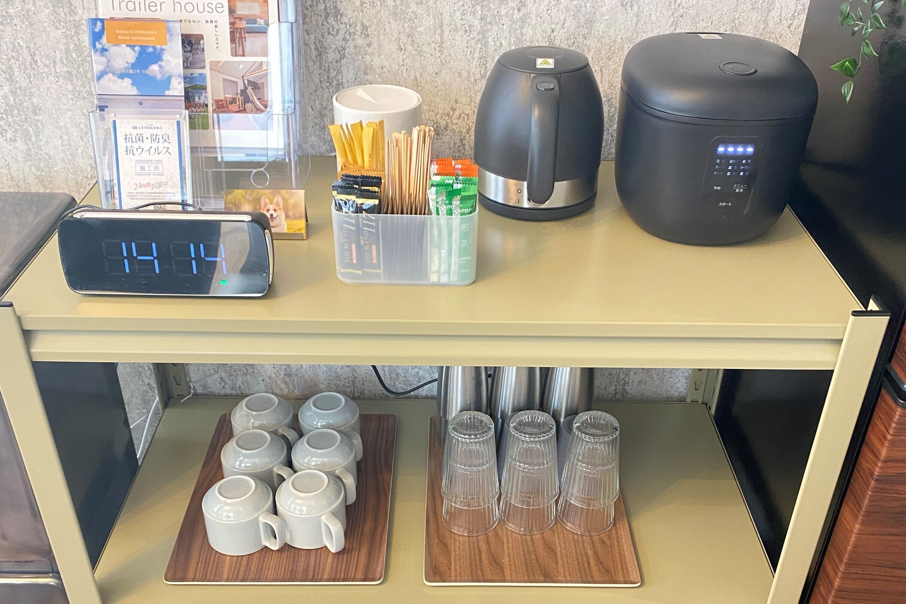 A kitchen counter with a coffee maker, a kettle, a clock, and a container with utensils.