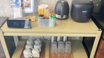 A kitchen counter with a coffee maker, a kettle, a clock, and a container with utensils.