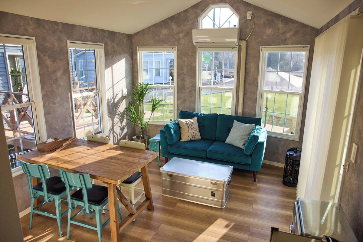 A living room with a wooden table, teal chairs, a teal sofa, and a large window.