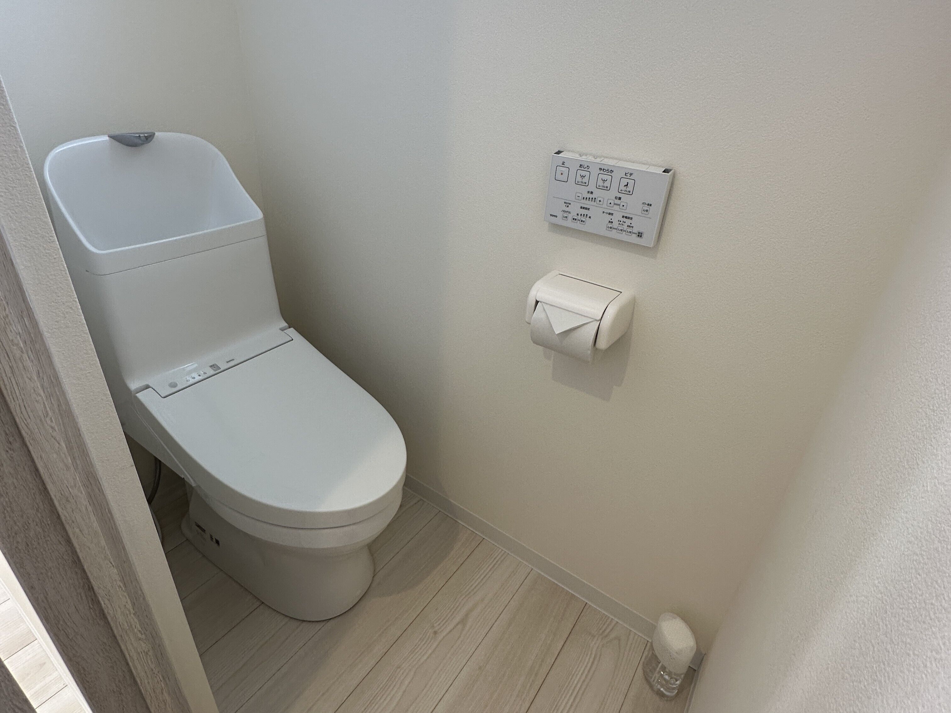 Inodoro blanco con botón de descarga y dispensador de papel higiénico en la pared.
