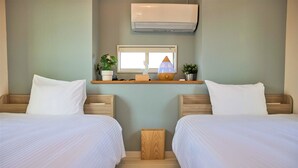 A hotel room with two beds, a small wooden nightstand, a window, an air conditioner, and a shelf with a plant and a decorative item.