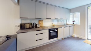 A modern kitchen with white cabinets, a built-in oven, a dishwasher, and a window providing natural light. - Oxford Bolthole | Oxford Holiday Let | 2 Beds & Sleeps 4 (Oxford)