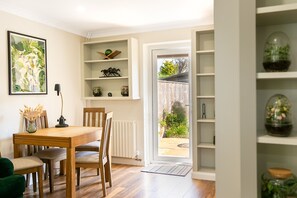 Ein Essbereich mit einem Holztisch und Stühlen, einer Vase mit getrockneten Blumen und einem gerahmten Bild an der Wand.