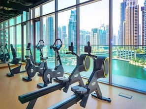 Et fitnesscenter med løbebånd og andet træningsudstyr, samt udsigt over bybilledet gennem store vinduer.
