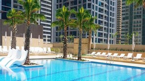 Una piscina con sillas de descanso y palmeras, rodeada de edificios altos.