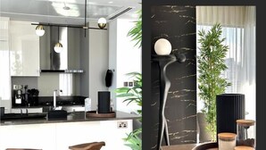 Una cocina moderna con una isla central, taburetes de bar, iluminación colgante y una pared de acento de mármol negro.