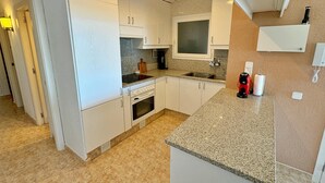 Eine moderne Küche mit weißen Schränken, einer Granit-Arbeitsplatte, einem eingebauten Backofen, einer Mikrowelle und einer Kaffeemaschine.