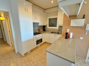 A modern kitchen with white cabinets, a granite countertop, a built-in oven, a microwave, and a coffee machine.