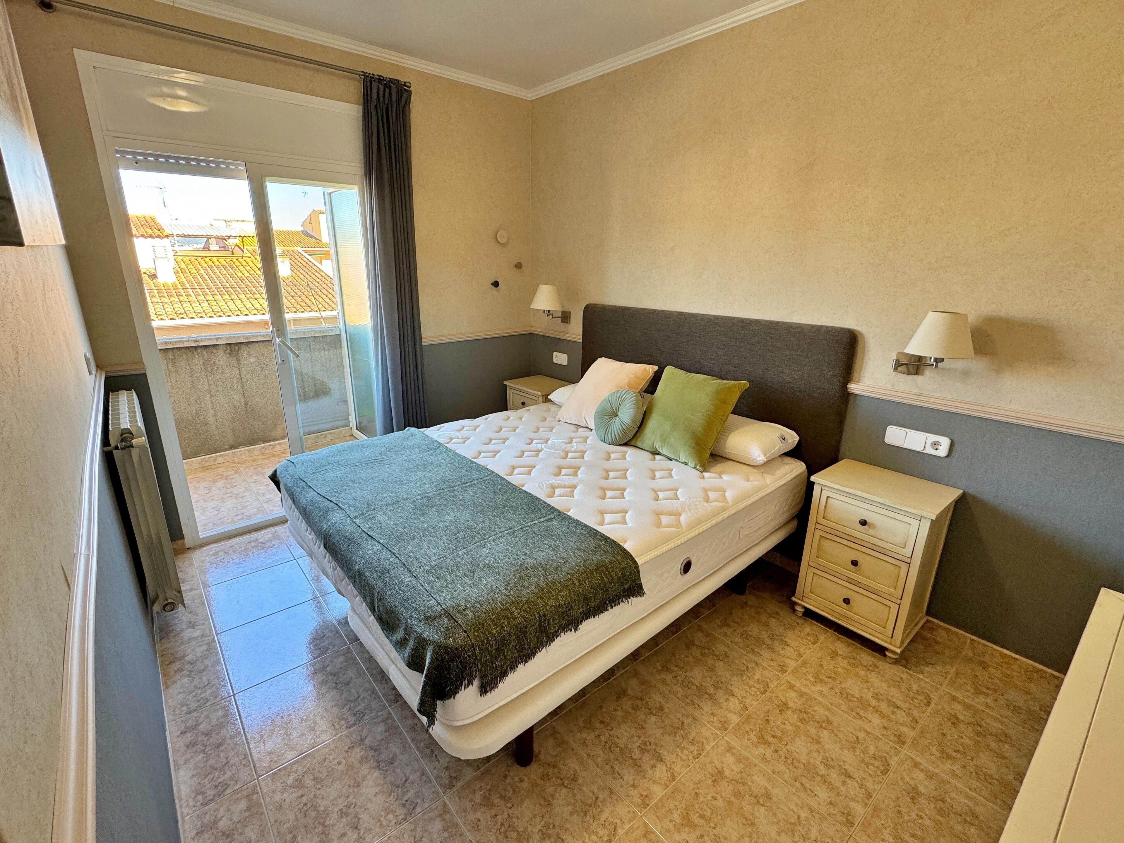 Un dormitorio con cama, dos mesitas de noche, una lámpara y vistas al exterior.