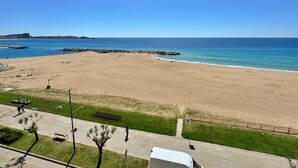 Ein Strand mit freiem Blick auf den Ozean, einem gepflasterten Weg und einer Rasenfläche mit einer Bank.