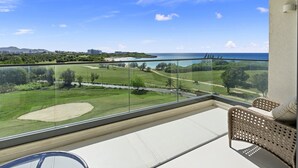 A balcony with a view of a golf course, ocean, and distant buildings.