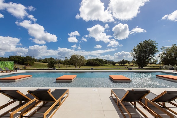 A pool with lounge chairs and a view of the sky and trees.