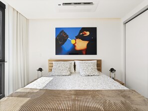 Ein modernes Schlafzimmer mit einem hölzernen Kopfteil, einer gemusterten Bettdecke und einem großen abstrakten Gemälde an der Wand.