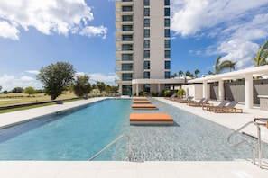 A swimming pool with steps leading into the water, surrounded by lounge chairs and a tall building in the background.