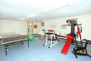 Une salle de sport équipée de matériel d’exercice, d’une table de ping-pong et d’un ballon d’exercice vert.