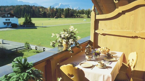 Ein Balkon mit Esstisch, mit Blick auf ein grünes Feld und Berge.
