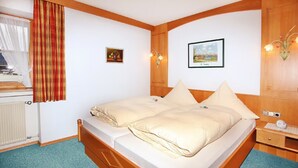 Ein ordentlich bezogenes Bett mit Kissen, ein hölzernes Kopfteil, ein kleiner Nachttisch mit Lampe und ein gerahmtes Bild an der Wand.