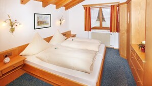 A bedroom with a wooden bed, a nightstand, a wall-mounted light, a framed picture, and a window with curtains.