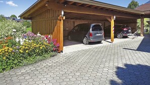 A covered garage with two cars parked inside, a paved driveway, and a garden with various flowers.