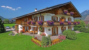 A two-story chalet with wooden balconies, flower boxes, and a stone foundation.