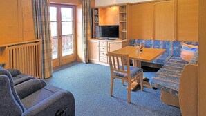 A compact room with a sofa, a table, a television, and a window with curtains.