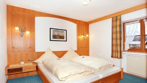 A room with a bed, a nightstand, a wall-mounted picture, and a window with curtains.