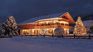 A snow-covered building with a balcony, surrounded by snow-covered trees and a fence.