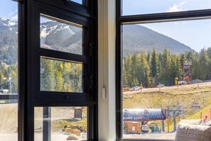 A window with a view of a mountainous landscape, a construction site, and a small building with a sign.