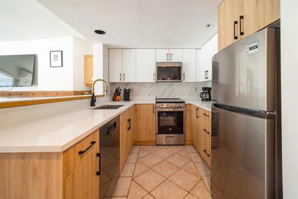 Una cocina moderna con gabinetes blancos, un refrigerador de acero inoxidable y suelo de baldosas.