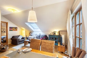 A cozy loft-style living space with a high ceiling, a dining area, and a view of the sky through a skylight.