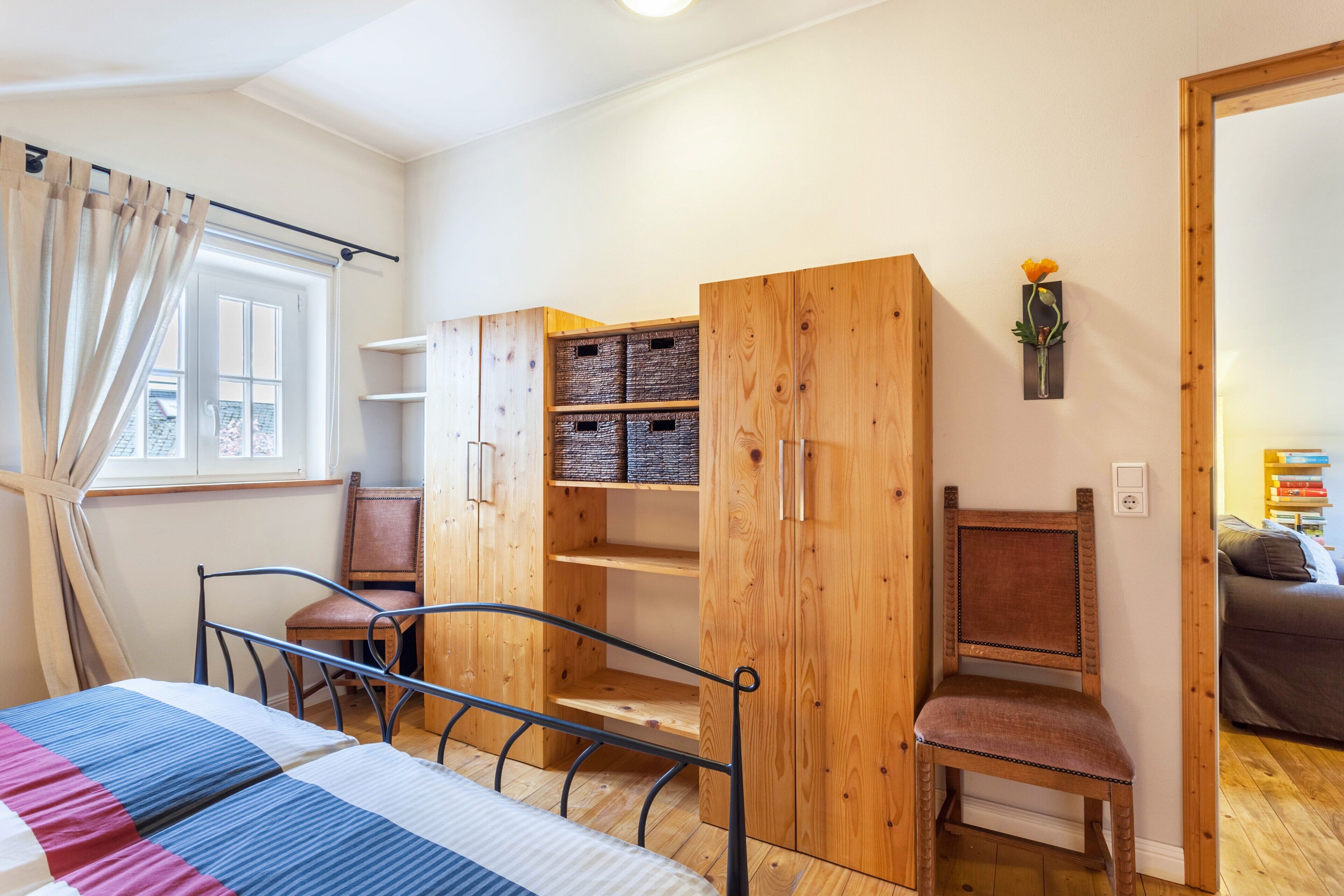 A bedroom with a bed, wooden wardrobe, chair, and a window with curtains.