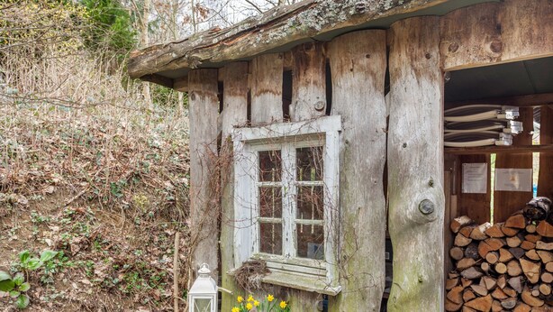 Une cabane en bois rustique, dotée d’une fenêtre, d’une nichoir, d’une lanterne et d’un pot de fleurs.