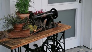 A vintage sewing machine on a wooden table with potted plants in front of a white door.