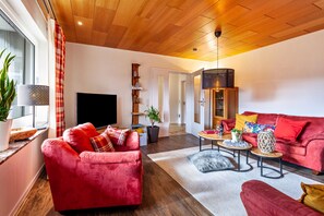 Una sala de estar moderna con un sofá rojo, un televisor y un techo de madera.