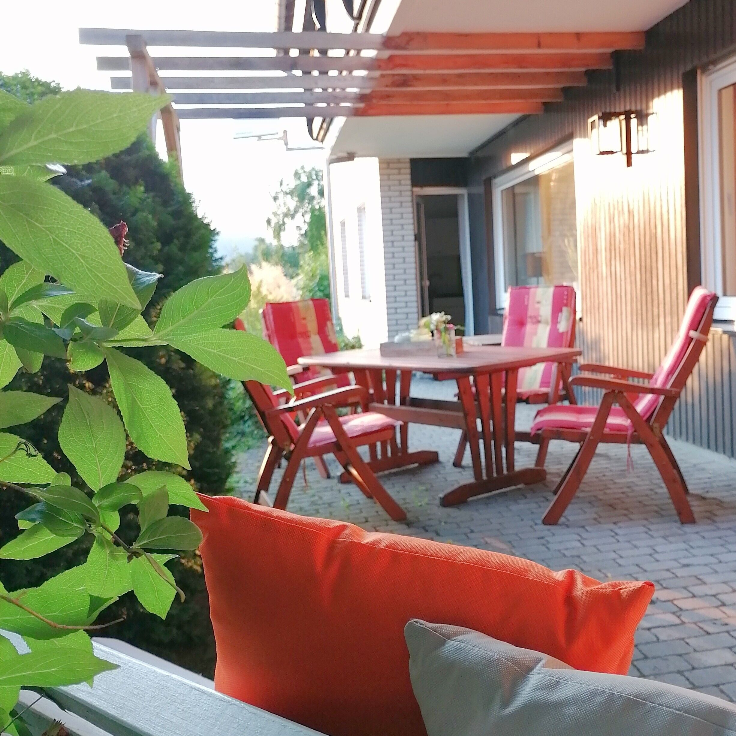 An outdoor patio with a table and chairs, surrounded by greenery.