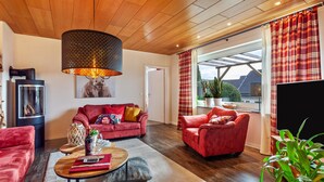 A living room with a red sofa, a coffee table, a fireplace, and a large window with curtains.